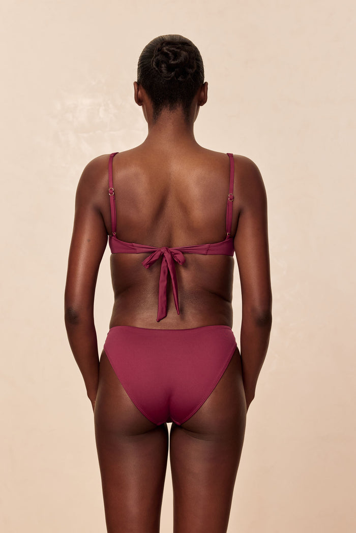 Rear view of Cala Roja Top in Fig on model showcasing adjustable straps and tie-back closure with beige background