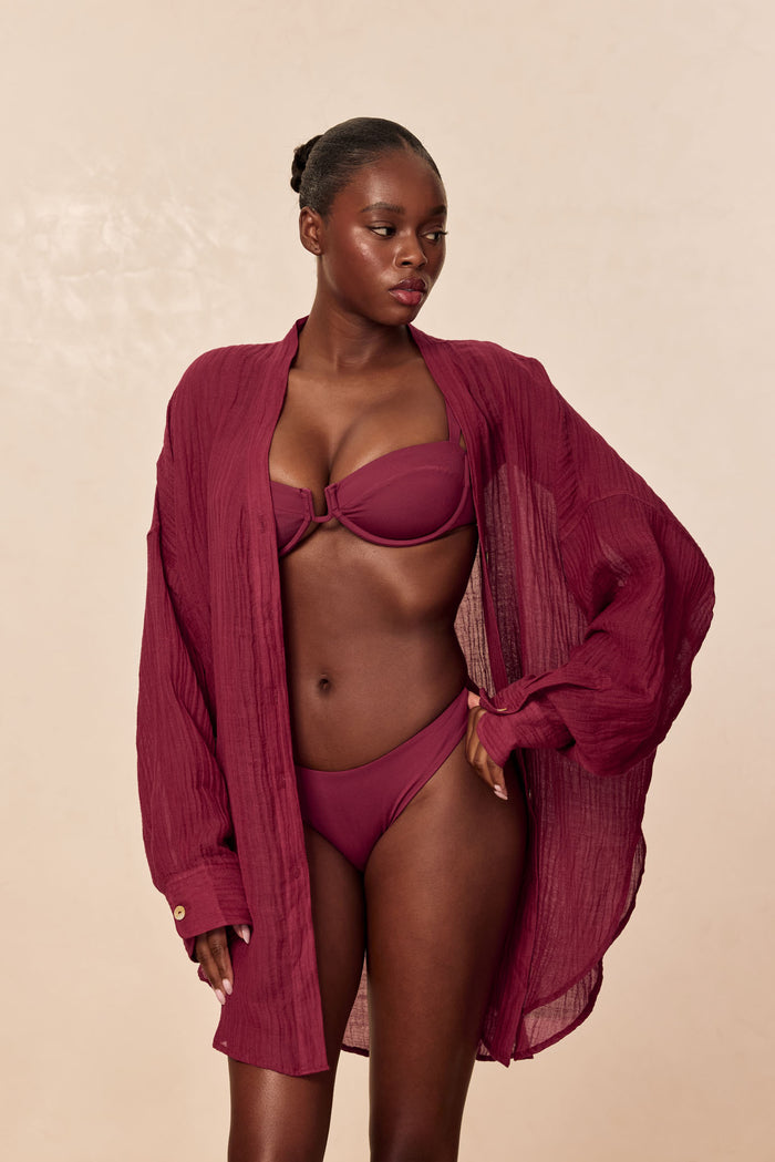 Three-quarter front of Cala Roja Top in Fig showing balconette underwire and center clasp on model against a beige background