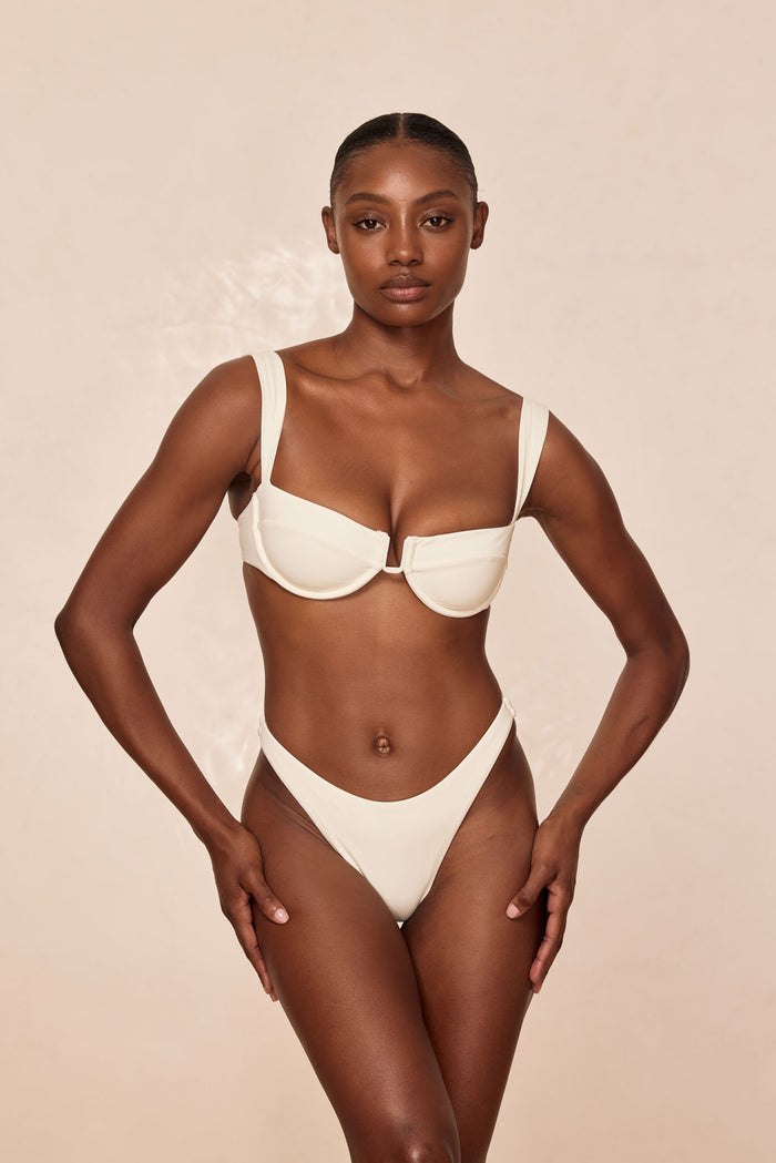 Front view of Byron Thong in ivory showcasing high-cut V-front and minimal coverage with a neutral beige background