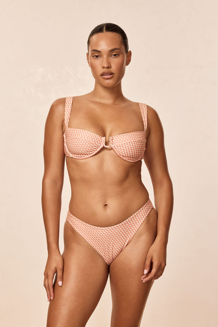 Front view of Cala Roja Top in peach micro-geo with balconette underwire and center ring on beige background