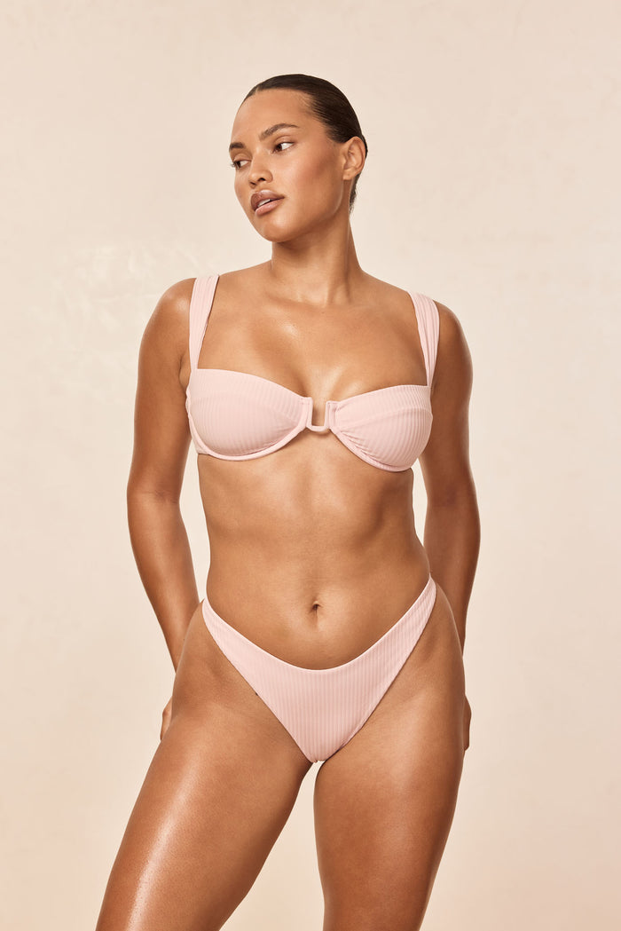 Front view of Cala Roja Top in powder pink rib, showing underwire cups, wide straps, ribbed texture on beige background