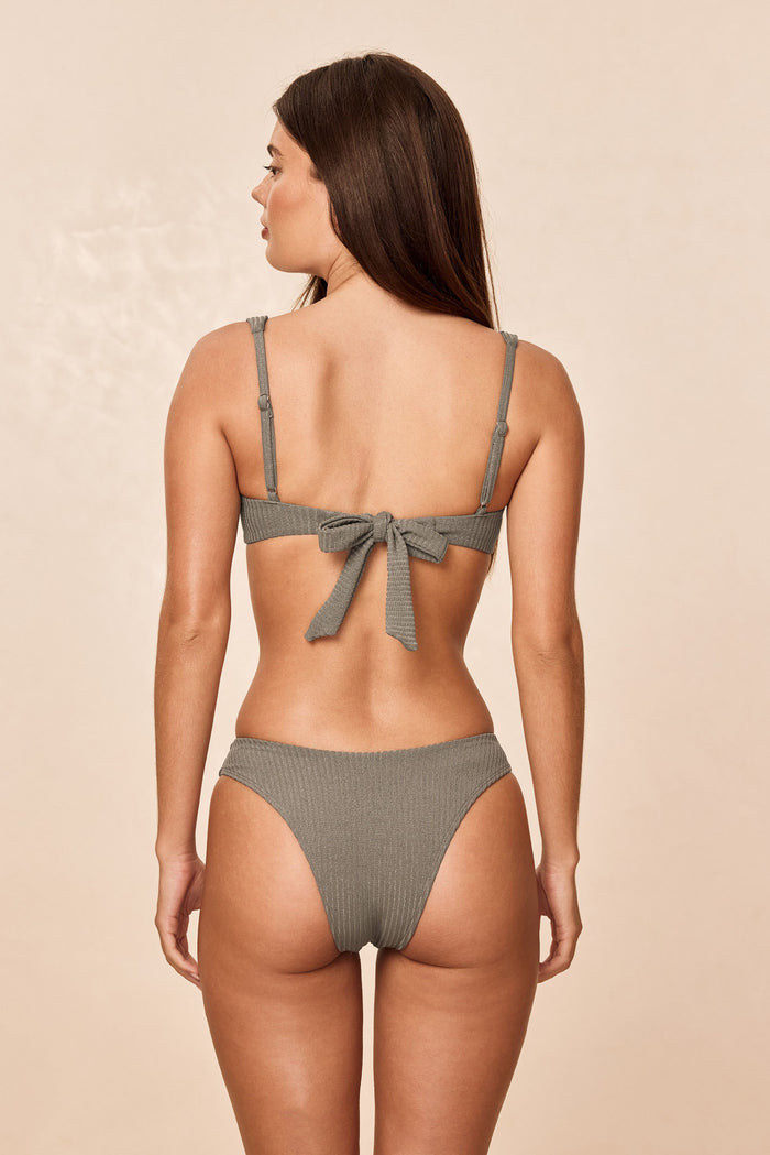 Back view of Cala Roja Top in Steel Lurex Rib showcasing adjustable straps and tied back bow on model against neutral background