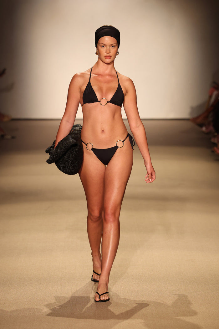 Front view of Cannes Bottom in black on a model showing gold ring hip details and low rise tie sides on runway