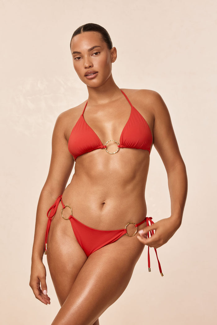 Three-quarter view of Cannes bottom in Chili Pepper on model, showing low-rise tie sides with gold ring accents on a neutral background