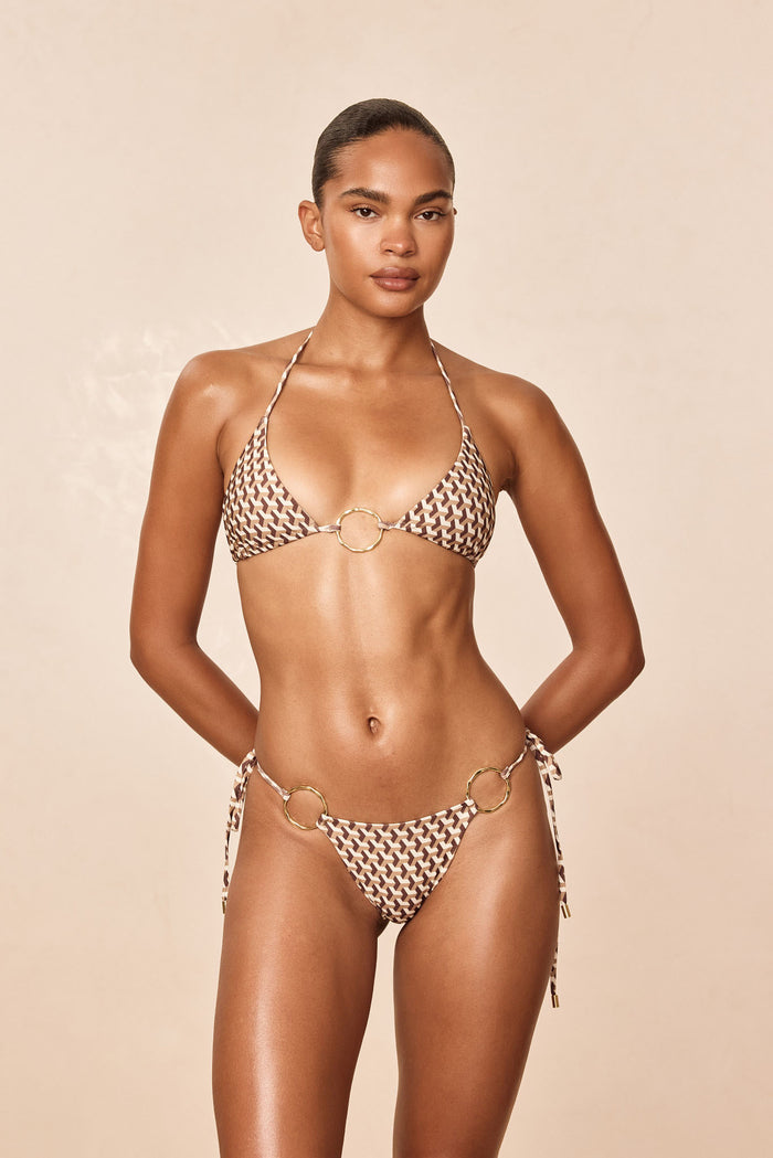 Front view of Cannes Bottom Husk Geo on model highlighting low-rise tie-side cut, brown geometric print, and gold ring hardware on beige background