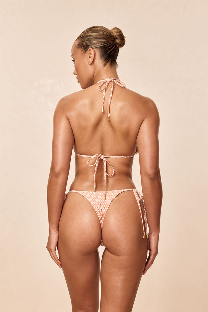 Rear view of Cannes bottom in Micro Geo print showing cheeky coverage and side-tie straps on model against a beige background