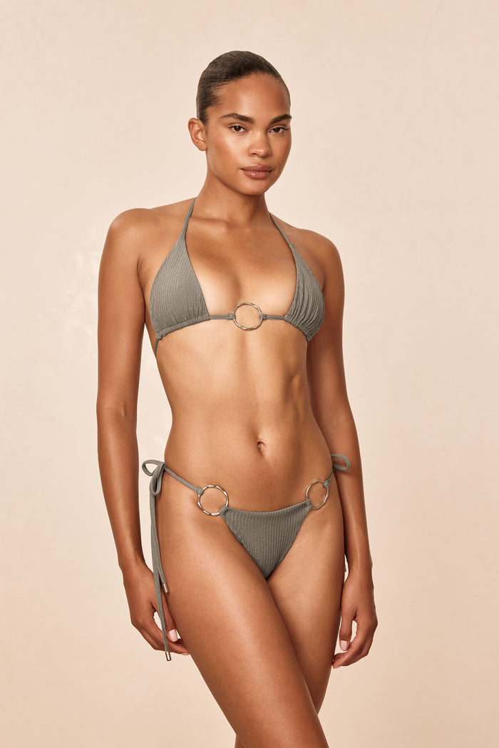Front three-quarter view of Cannes bottom in steel lurex rib with ribbed texture, side ties, and metal ring detail on beige background