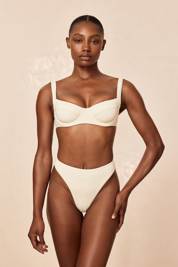 Front view of Capri Thong in ivory showcasing high-rise, high-cut thong silhouette on model against beige background