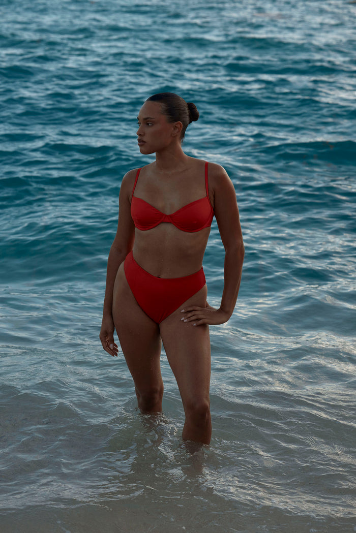 Front view of Capri Top in Chili Pepper red showing underwire cups and adjustable straps on model standing in the ocean