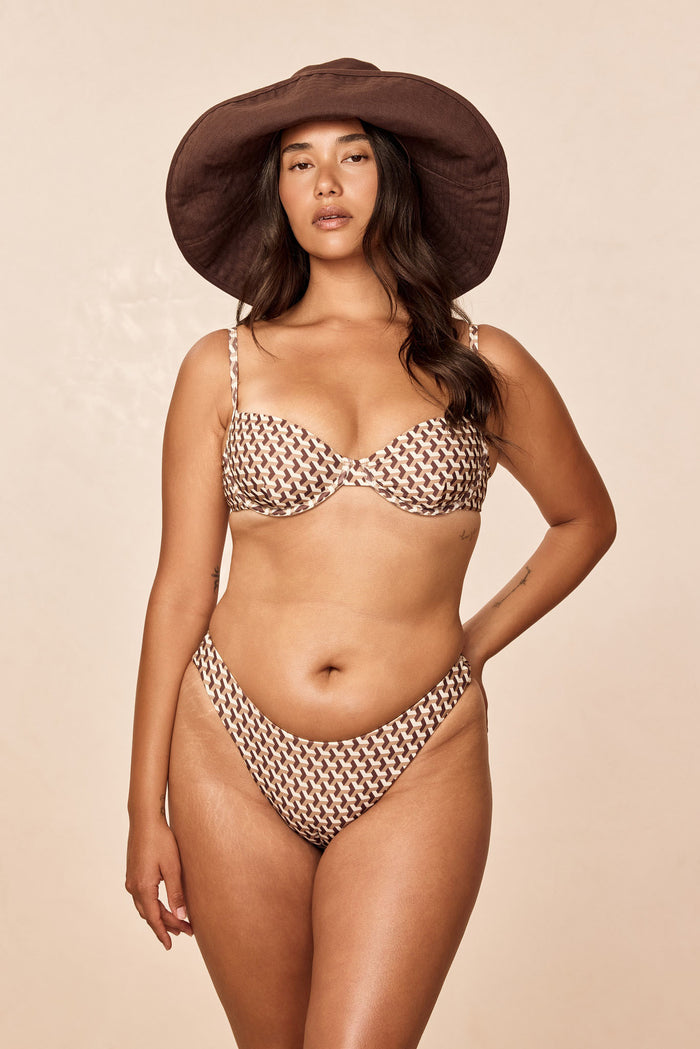 Front view of Capri Top - Husk Geo on model showing brown-and-cream geometric underwire cups and thin adjustable shoulder straps on a neutral beige background