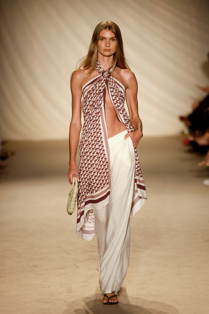 Front view of Marina Piccola Sarong - Husk Geo showcasing brown-and-white geometric print tied halter with ring and high side slit on a beige runway
