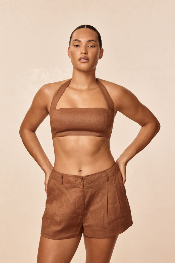 Front view of Casablanca short in caramel linen showing high-rise button-front shorts with pleats on a model against a beige backdrop