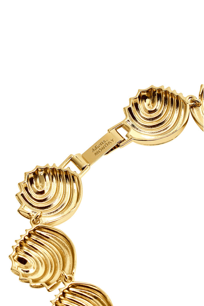 Gold shell-link necklace showing scalloped shell charms and rectangular clasp engraved 'MONDAY'