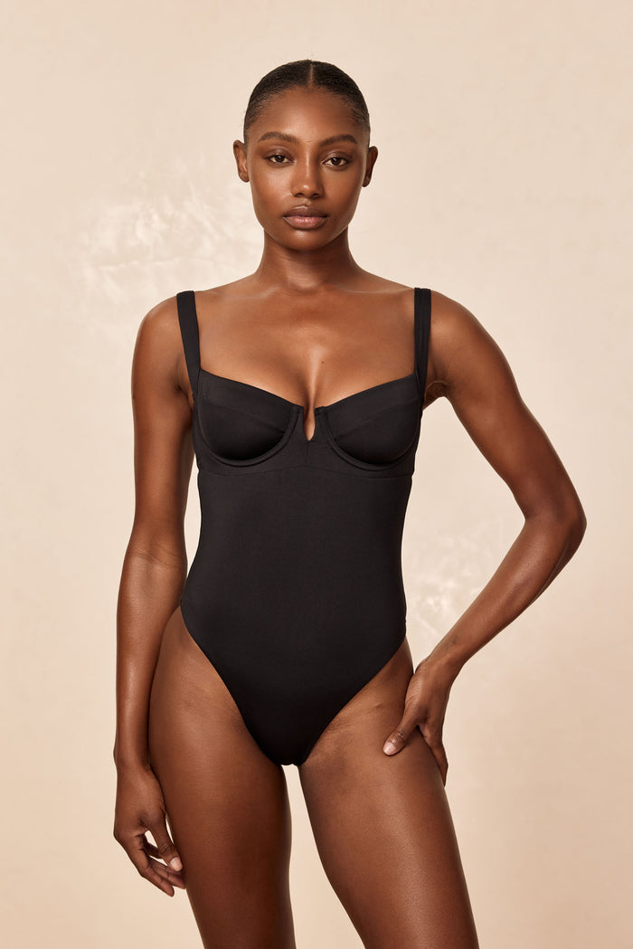 Front view of Clovelly one-piece swimsuit in black with underwire cups, square neckline, high-cut leg on beige background