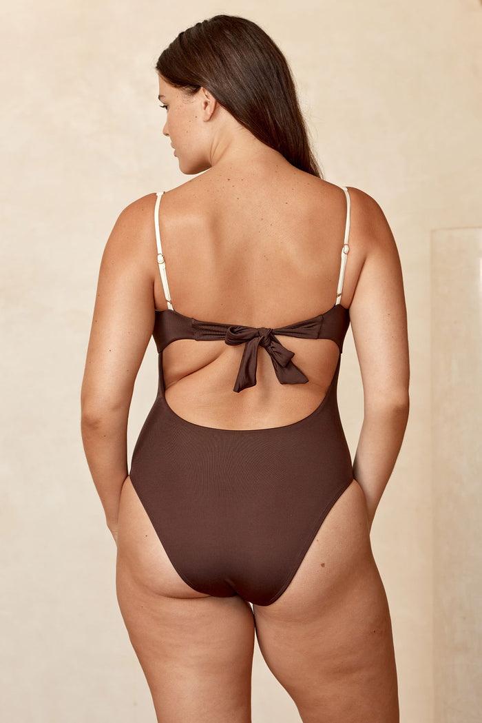 Rear view of Clovelly One Piece in espresso and ivory showcasing tied bow back, adjustable ivory straps and scoop back on beige backdrop