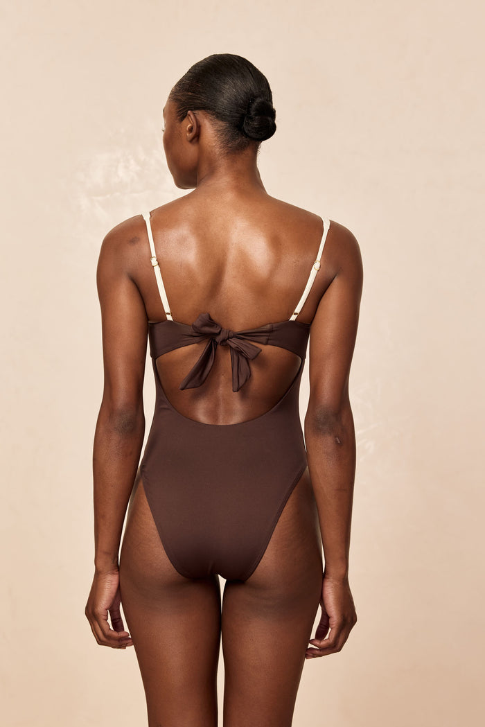 Rear view of woman wearing brown one-piece swimsuit with bow tie back and cream adjustable straps