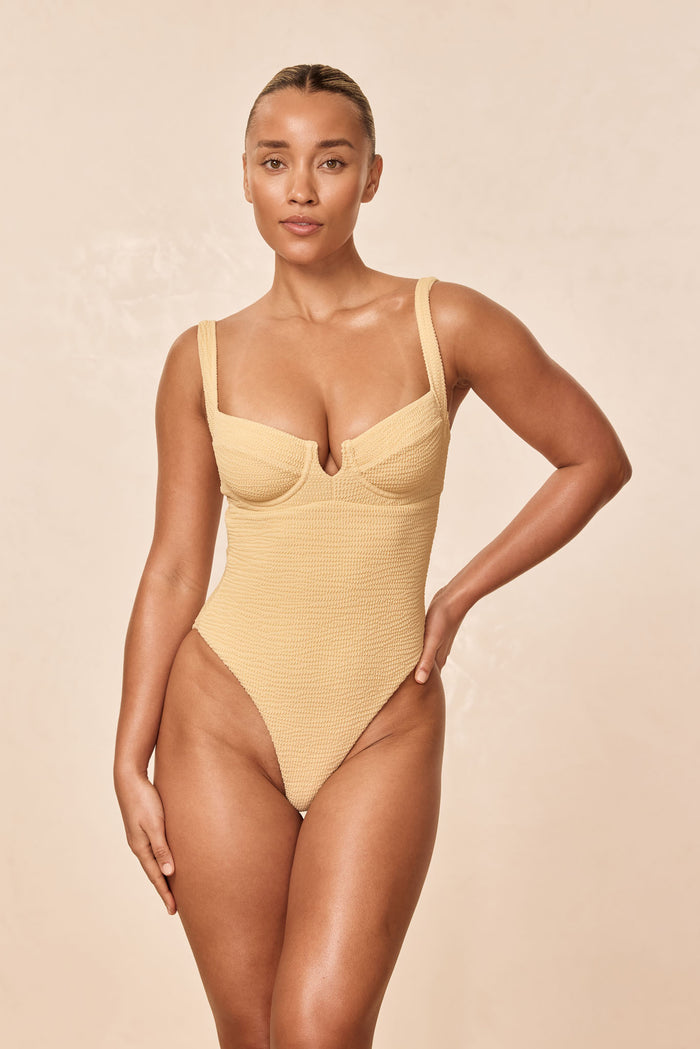 Front view of Clovelly One Piece in Raffia Crinkle on model showing underwire cups and high-leg cheeky cut, pale beige background