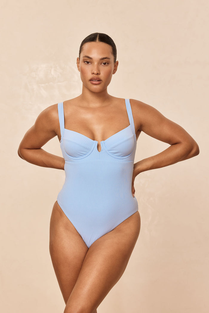 Front of Clovelly one-piece in Sky Rib showing ribbed fabric, underwire cups with keyhole and high-cut leg on beige background