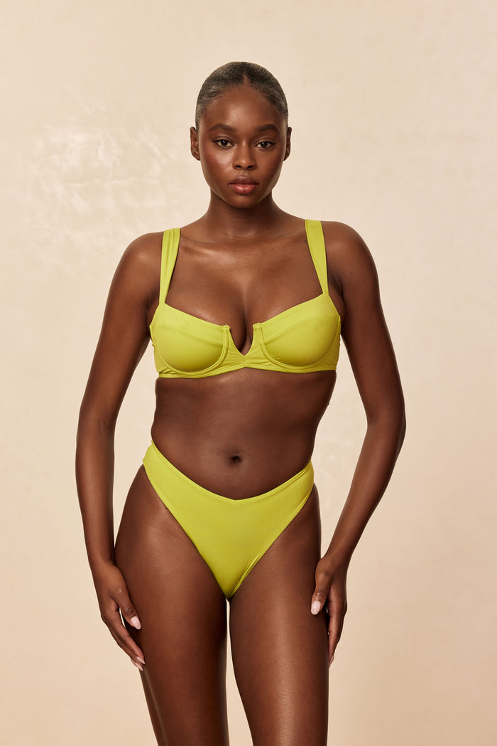Front view of Clovelly Top in Apple on model, showing underwire cups, V-notch center and wide straps on beige background