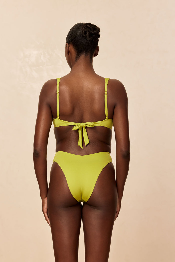 Back view of Clovelly Top in Apple on model showing tie-back closure and adjustable shoulder straps on a neutral beige studio background