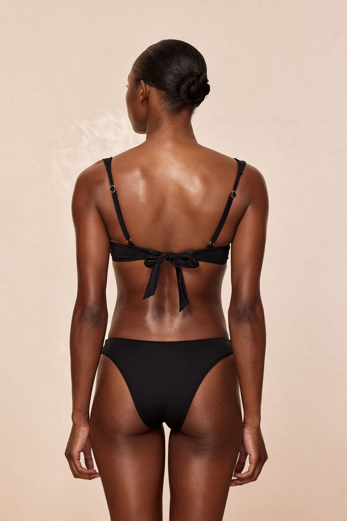 Back view of Byron Bottom in black on model showing mid-rise fit and moderate rear coverage against beige background