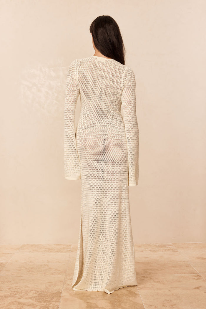 Back view of Corossol dress in ivory crochet, showing long fitted sleeves and sheer ankle-length skirt with side slit on neutral background