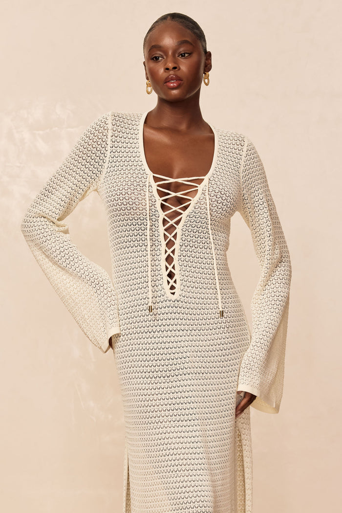 Front view of Corossol Dress in ivory lace crochet on model showcasing lace-up V neckline, bell sleeves and side slit on beige background