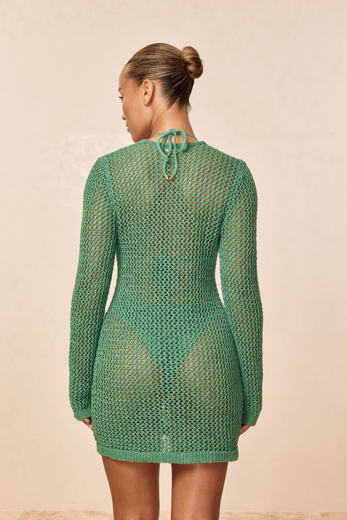 Back view of Corossol Mini Dress in Pond Petit Crochet showing open crochet knit, long sleeves on beige background