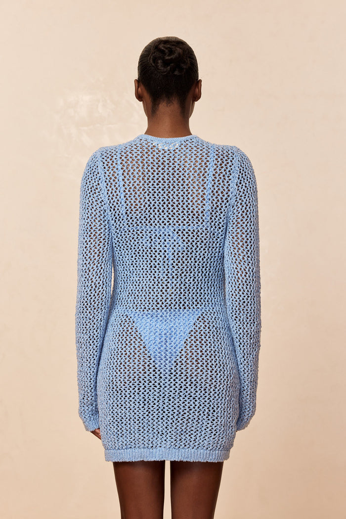 Back view of Corossol mini dress in sky petit crochet, sheer open-knit long sleeves and bikini underlay on beige background