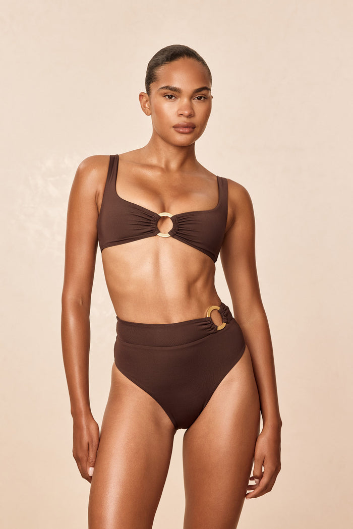Front of Costa Rica Bottom in Espresso on model, high-waisted full coverage with gold ring side detail on beige background