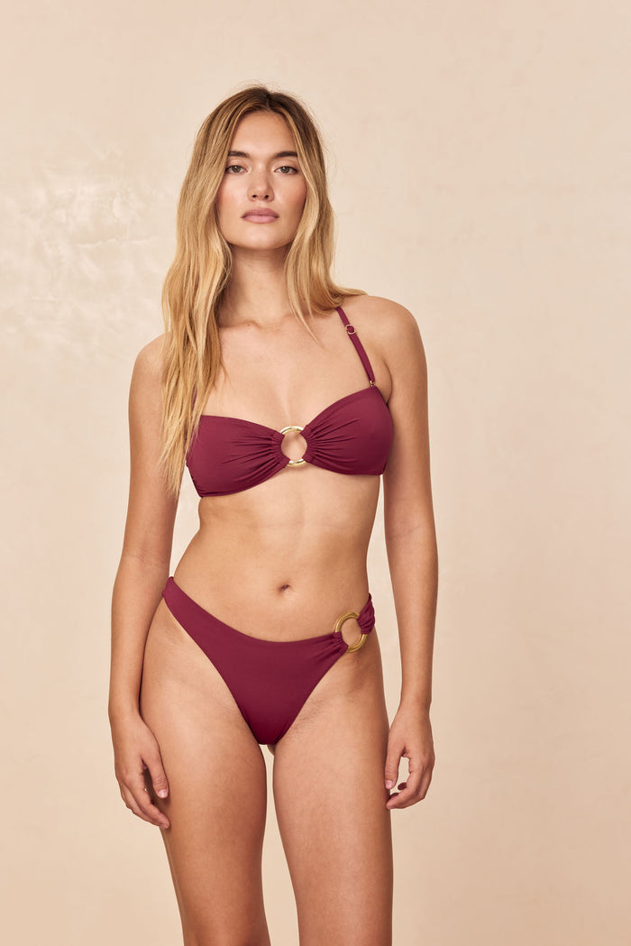 Front view of Costa Rica Top in Fig on model, bandeau with center gold ring and adjustable halter strap on beige background