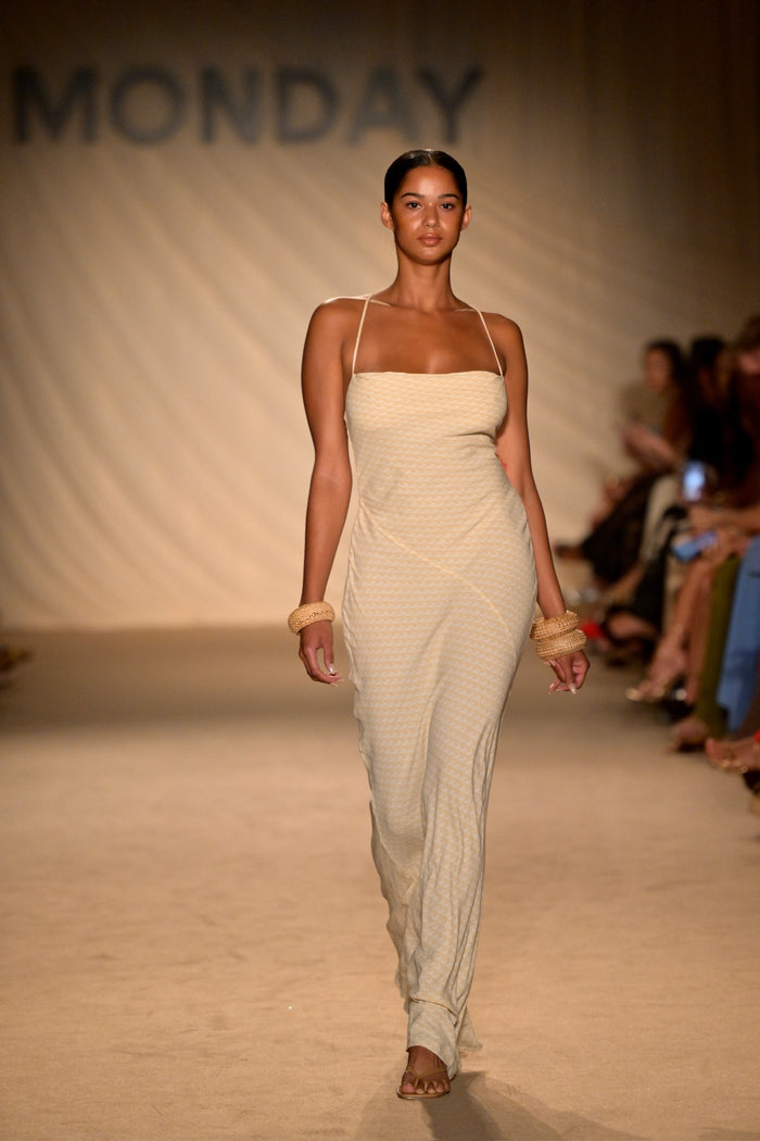 Front view of Cote D’azur Dress in Ivory Geo with spaghetti straps, woven bracelets and runway backdrop reading MONDAY