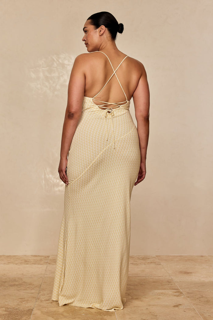 Back view of Cote D’azur Dress in Ivory Geo with crisscross spaghetti straps, lace-up back, and fitted column skirt on beige backdrop