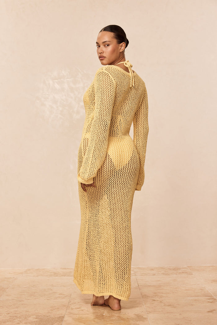 Three-quarter back view of Cozumel Dress in honey petit crochet, long-sleeve open-knit maxi over bikini on beige background
