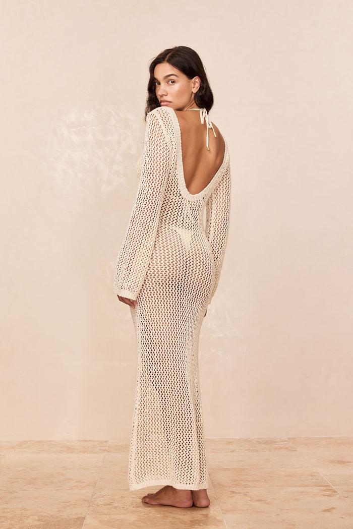 Rear view of Cozumel Dress in ivory crochet showing open scoop back and long sheer knit on model against beige background