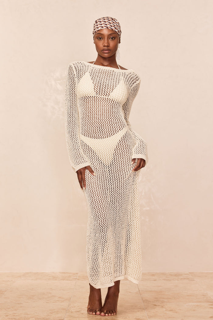 Model wearing Cozumel Dress, ivory petit crochet; open-knit long-sleeve ankle-length dress with boat neckline on neutral background
