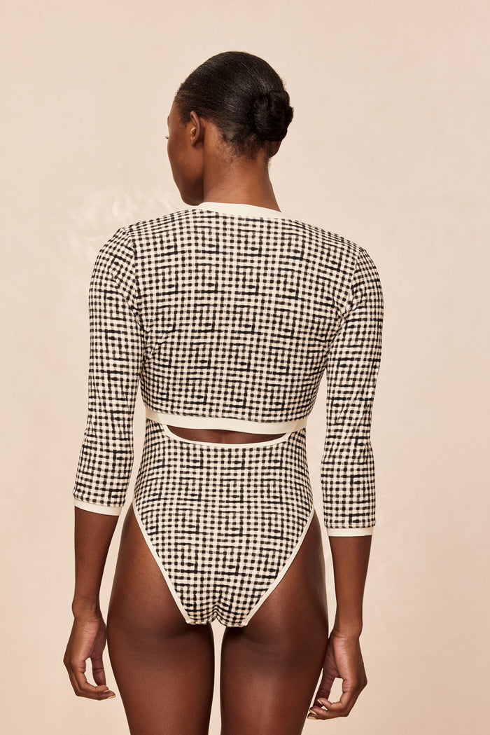 Back view of Crete Swim Cardi in black gingham showcasing back cutout and cream trim with neutral beige backdrop