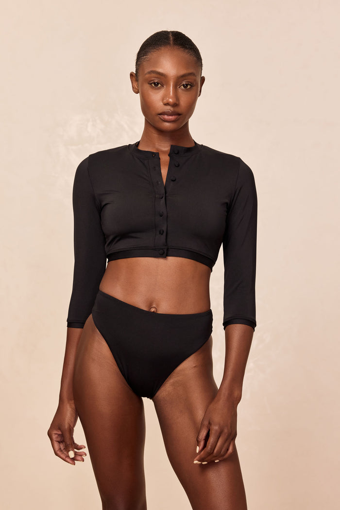 Front view of model in black cropped henley swim top with three-quarter sleeves and matching high-waist bikini bottoms.
