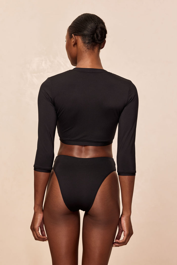 Rear view of Crete Swim Cardi in black showcasing cropped back and three-quarter sleeves on beige background