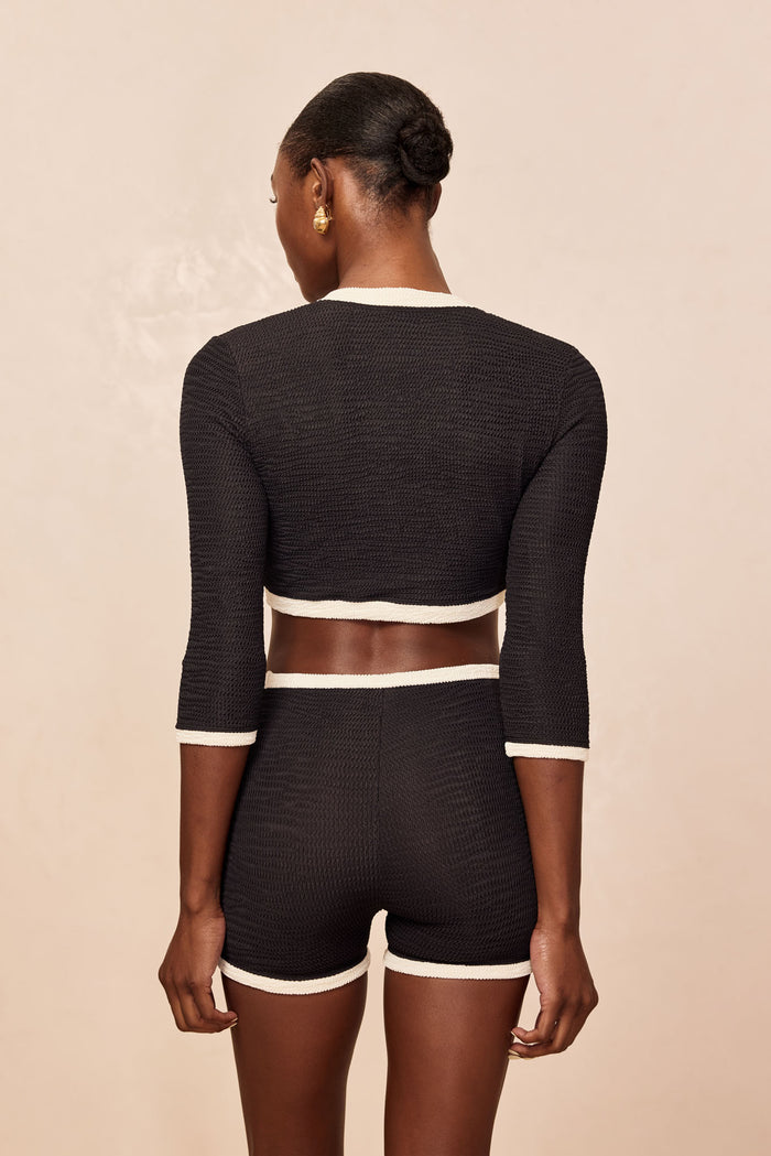 Back view of model wearing black textured cropped top and matching high-waist shorts with white trim.