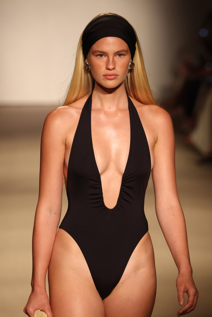 Front view of Croatia One Piece in black on model showcasing U-wire sheered halter plunge, high leg and cheeky coverage on runway