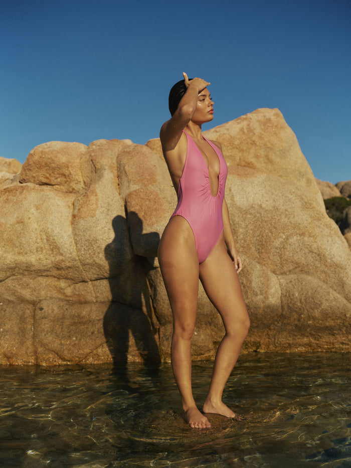 Side view of Croatia One Piece in Moonlight showing halter plunge, U-wire detail and high-leg cut on rocky shore