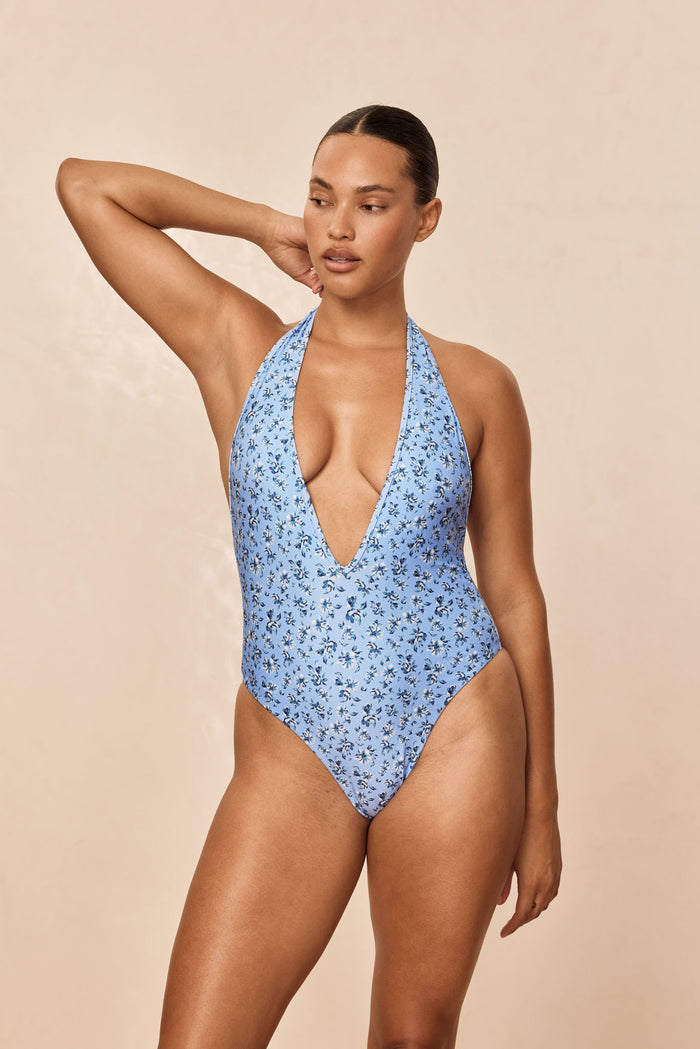 Front of Cyprus One Piece in Isola Floral light blue, halter plunge and high-leg cut on model against beige background