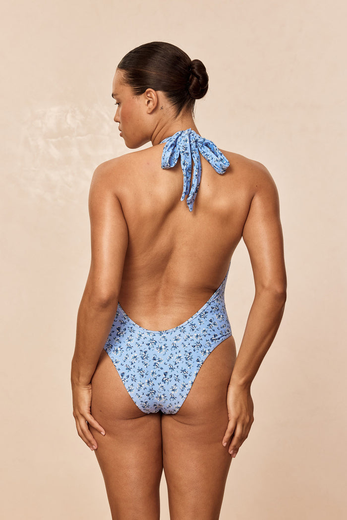 Back view of Cyprus One Piece showcasing halter tie, low scoop back and high-leg cheeky coverage on beige background