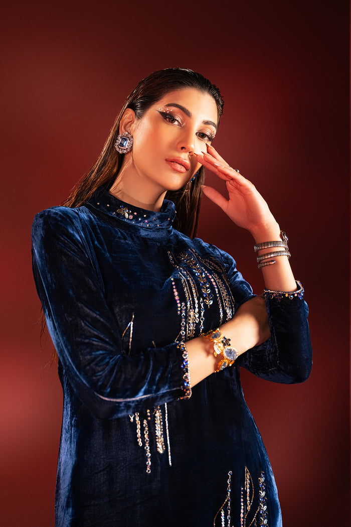 Seated pose of neon blue velvet formal outfit showing smooth fabric fall and structured trousers styling, polished ready to wear evening dress.