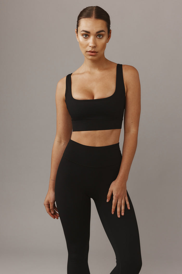 Front view of Devin Bra in black on model showcasing square neckline, wide straps, and elastic underband against gray backdrop