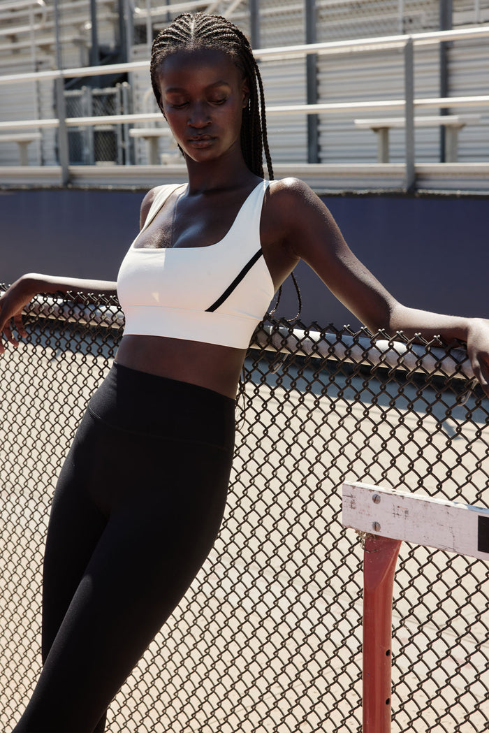 Front view of Devin Bra in ivory with black trim showcasing square neckline and supportive band on model at outdoor track
