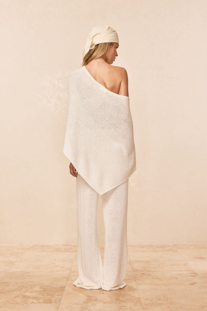 Rear view of Dominica Poncho in ivory showing open-knit fabric and asymmetrical one-shoulder drape on model against neutral background