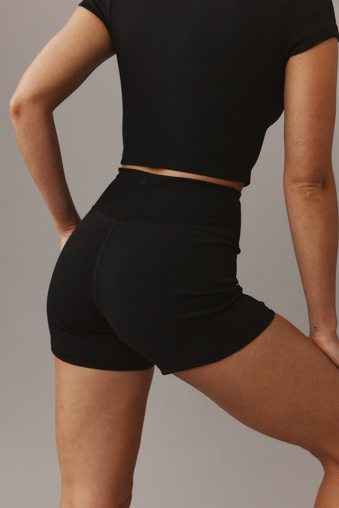 Rear view of Elysian Short 4.5-inch Black Lightweight Rib showcasing high waist, ribbed texture, and small embossed M on gray background
