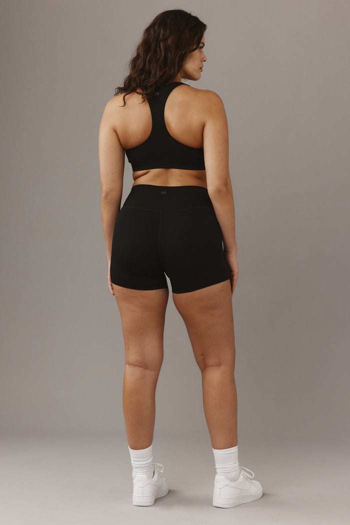 Rear view of Elysian Short 4.5in in black showcasing high‑waist fit and M logo on waistband with neutral gray background